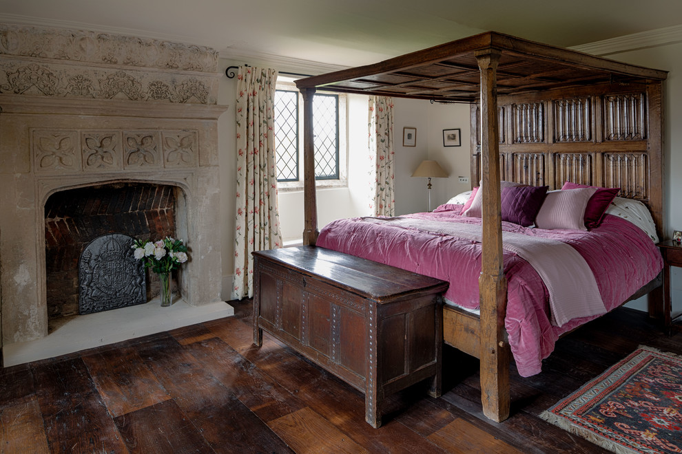 This is an example of a master bedroom in Wiltshire with dark hardwood flooring, a standard fireplace, a stone fireplace surround and brown floors.