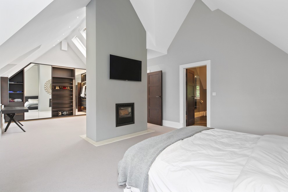 Example of a large trendy carpeted and gray floor bedroom design in Buckinghamshire with gray walls, a two-sided fireplace and a plaster fireplace