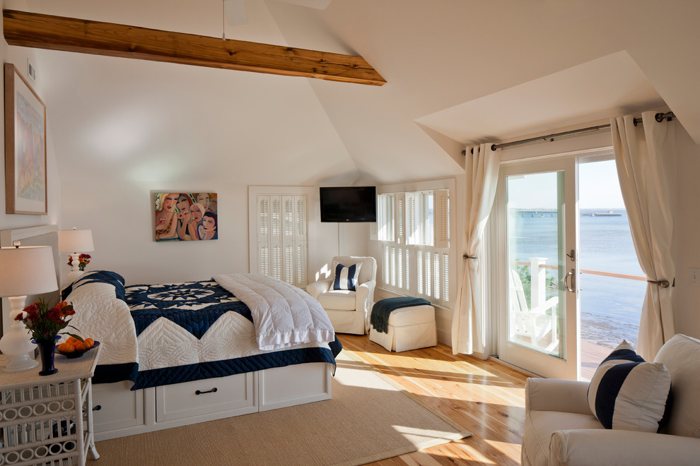 Ejemplo de dormitorio principal y televisión costero grande sin chimenea con paredes blancas, suelo de madera en tonos medios y suelo beige