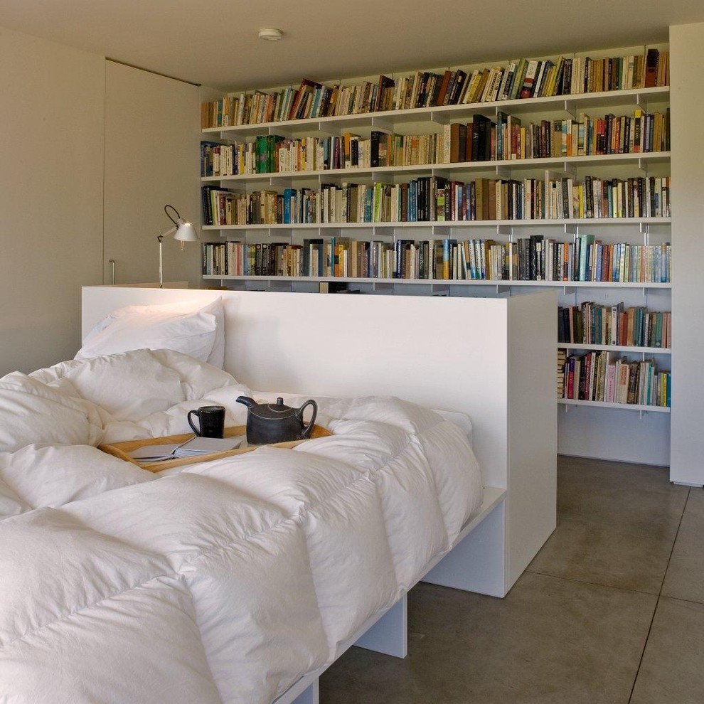 Modelo de dormitorio moderno con suelo de cemento, paredes blancas y con escritorio