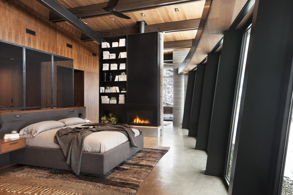 Idées déco pour une grande chambre parentale moderne avec sol en béton ciré, une cheminée standard, un manteau de cheminée en pierre et un sol gris.