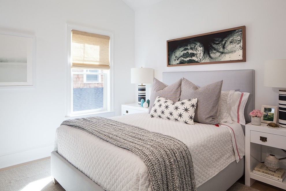 Diseño de dormitorio principal y gris y blanco costero con suelo de madera clara, marco de chimenea de piedra y paredes blancas