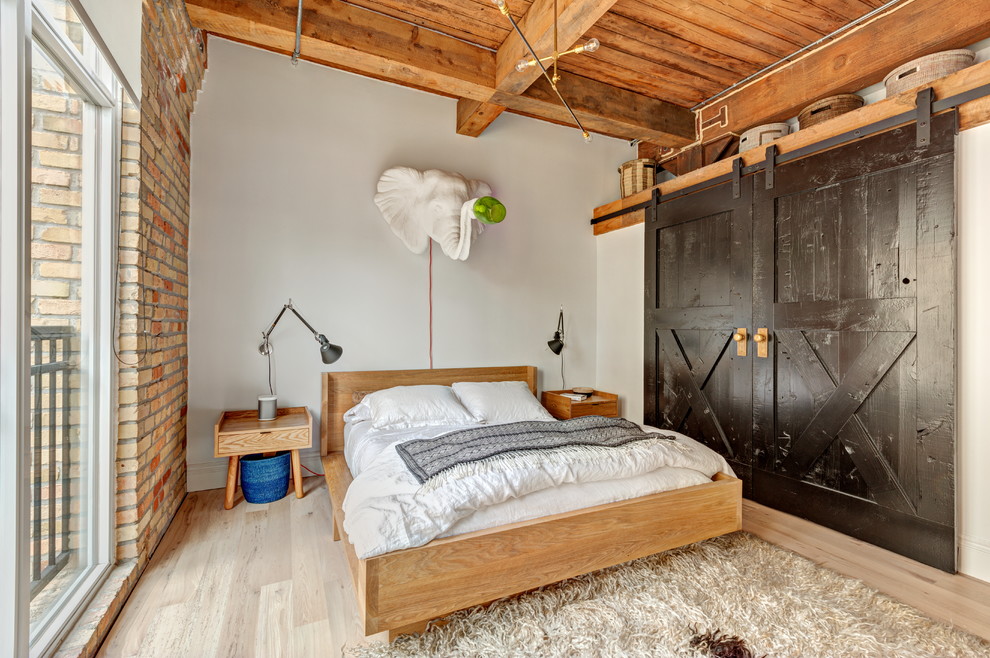 Ejemplo de dormitorio principal industrial de tamaño medio sin chimenea con paredes blancas y suelo de madera clara