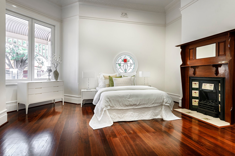 Пример оригинального дизайна: спальня в классическом стиле с белыми стенами, темным паркетным полом, фасадом камина из дерева и стандартным камином