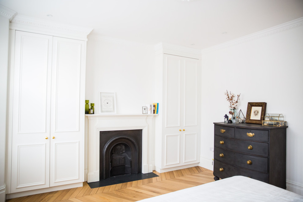 Cette image montre une chambre parentale minimaliste de taille moyenne avec un mur vert, parquet clair, une cheminée standard, un manteau de cheminée en métal et un sol marron.