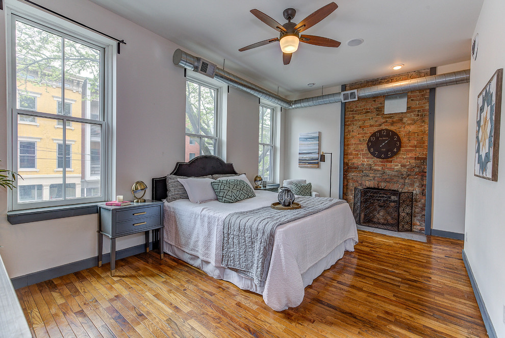 Inspiration for a medium sized urban master and grey and brown bedroom in Cincinnati with white walls, medium hardwood flooring, a standard fireplace, a brick fireplace surround and brown floors.