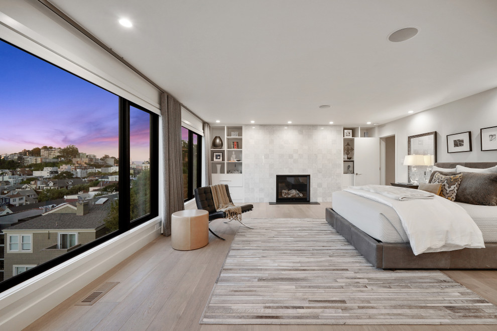Design ideas for a large contemporary master bedroom in San Francisco with white walls, light hardwood flooring, a tiled fireplace surround, beige floors and a standard fireplace.