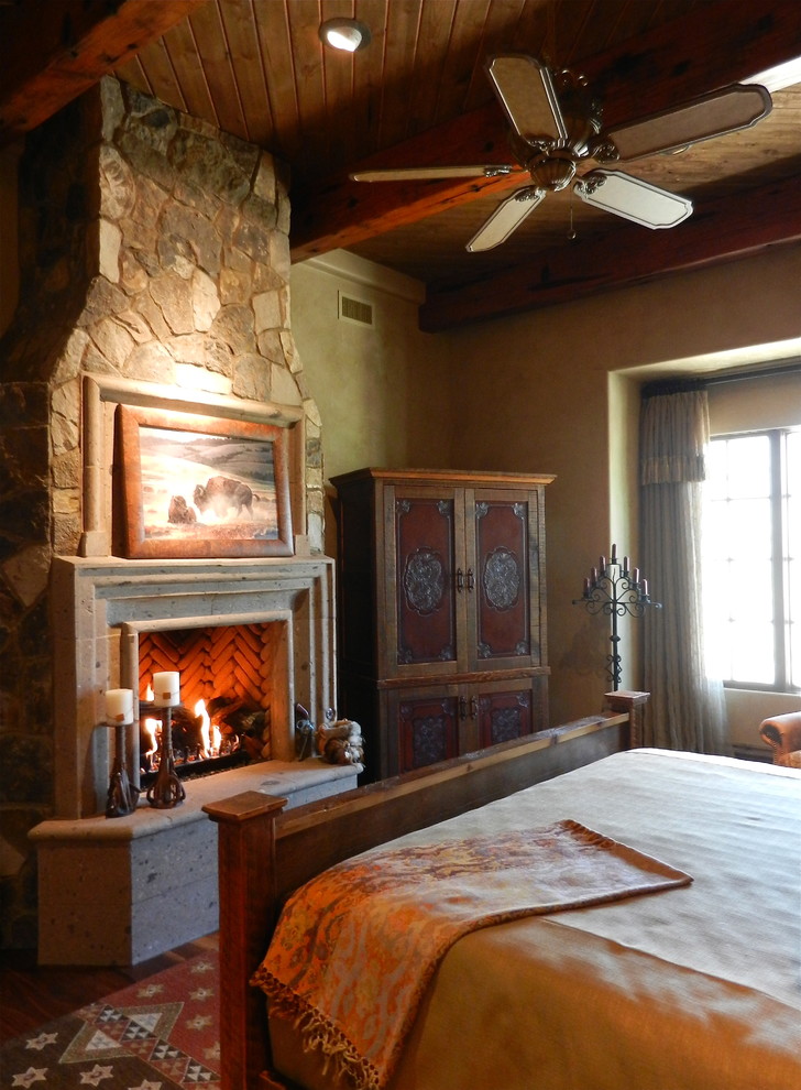 Imagen de habitación de invitados rural grande con paredes beige, suelo de madera en tonos medios, todas las chimeneas y marco de chimenea de piedra