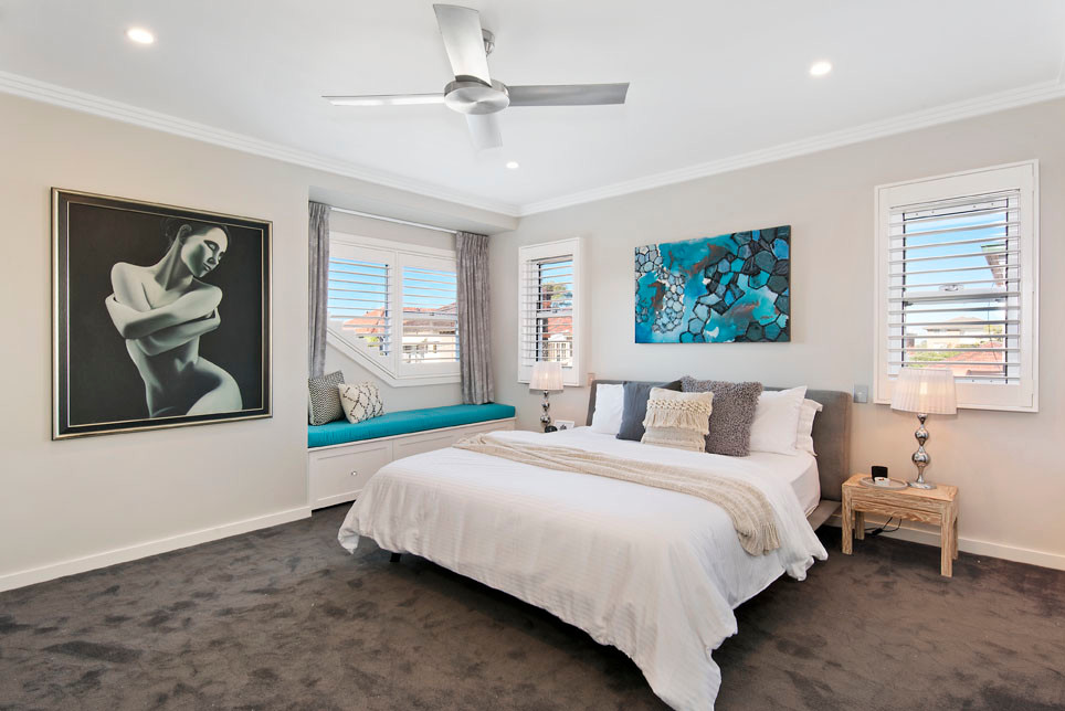 Large coastal master bedroom in Sydney with beige walls, carpet and grey floors.