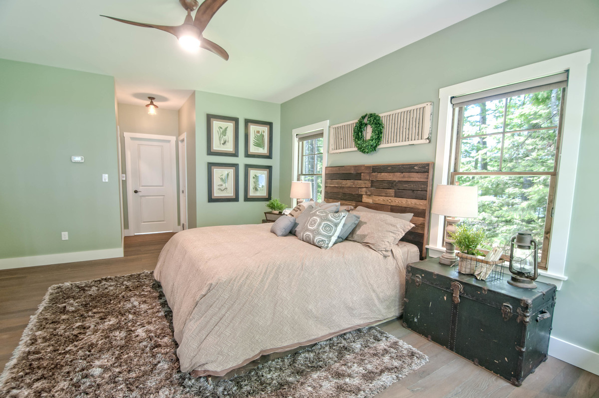 Cette image montre une grande chambre parentale craftsman avec un mur vert, un sol en bois brun et un sol marron.