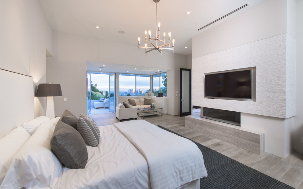 Modernes Hauptschlafzimmer mit weißer Wandfarbe, hellem Holzboden, Gaskamin, Kaminumrandung aus Beton und beigem Boden in Los Angeles