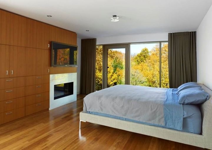Ejemplo de dormitorio principal actual grande con paredes beige, suelo de madera clara, chimenea lineal, marco de chimenea de baldosas y/o azulejos y suelo marrón