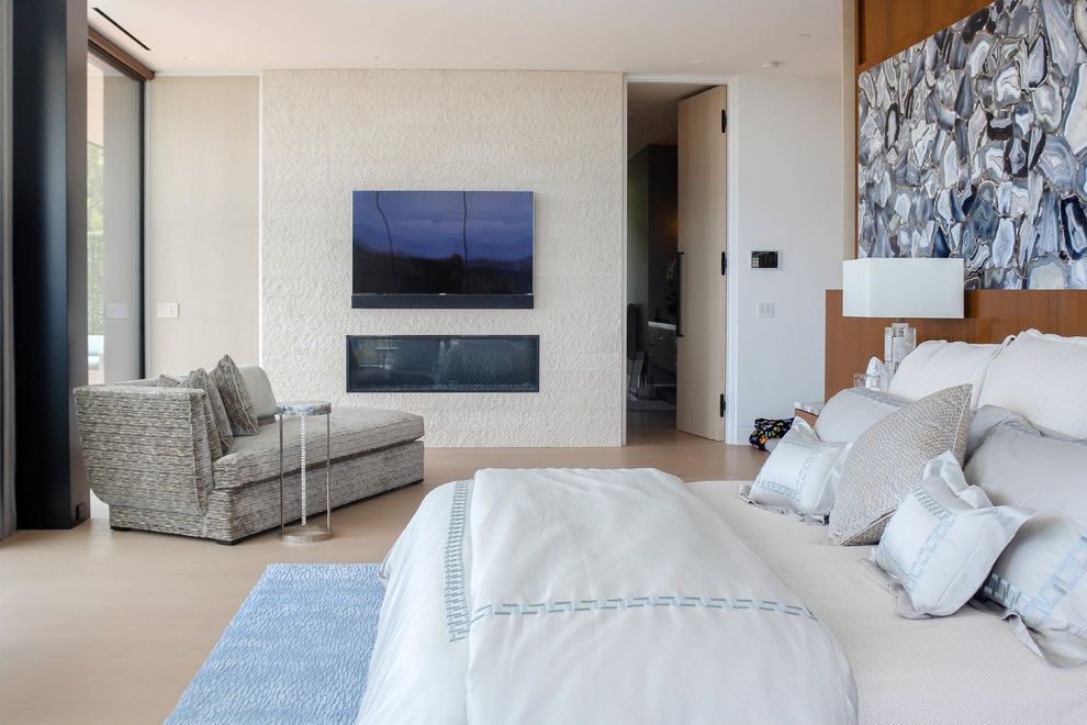 Imagen de dormitorio principal moderno grande con suelo blanco, paredes beige, suelo de madera clara, chimenea lineal y marco de chimenea de piedra