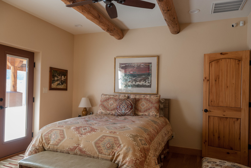 Modelo de dormitorio principal de estilo americano de tamaño medio con paredes beige, suelo de madera en tonos medios, suelo marrón y vigas vistas