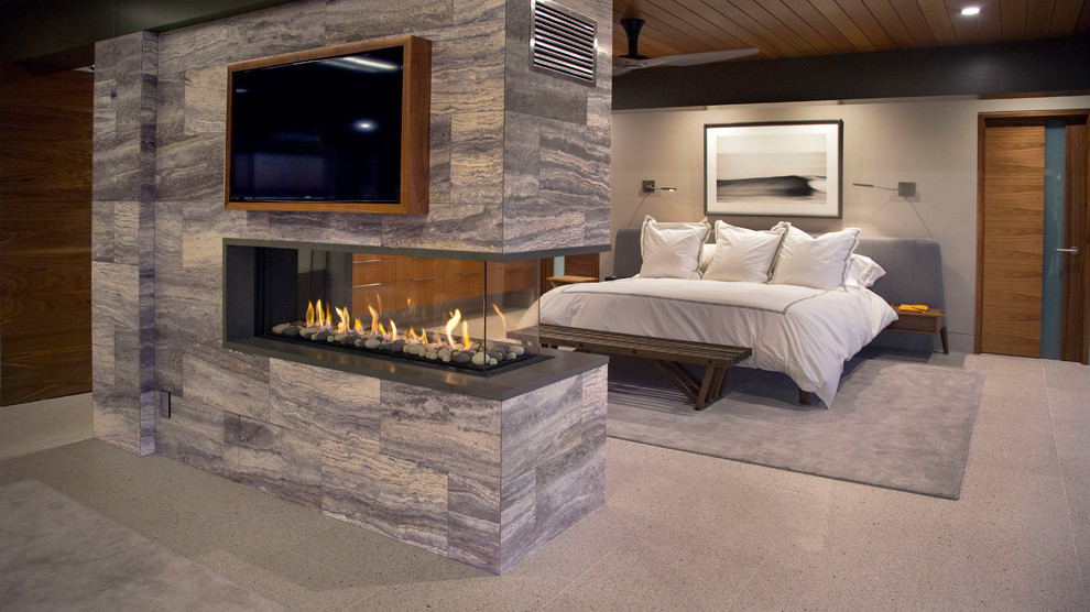 Cette photo montre une chambre tendance avec un mur gris, une cheminée double-face et un manteau de cheminée en pierre.