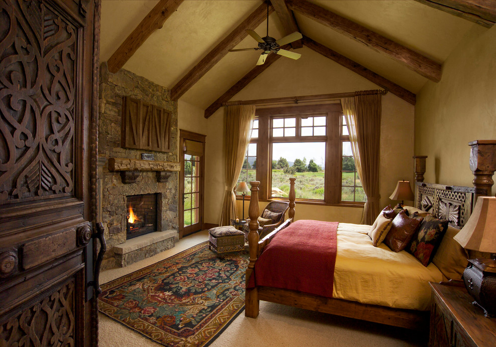 Großes Uriges Hauptschlafzimmer mit beiger Wandfarbe, Teppichboden, Kamin, Kaminumrandung aus Stein und beigem Boden in Denver