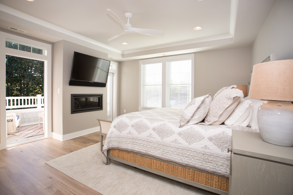 Ejemplo de dormitorio principal y televisión marinero grande con paredes beige, suelo de madera clara, chimenea lineal y suelo beige