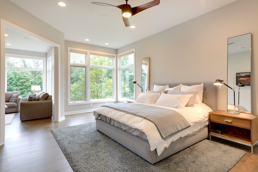 Photo of a large contemporary master bedroom in Minneapolis with white walls, dark hardwood flooring, a two-sided fireplace, a tiled fireplace surround and brown floors.