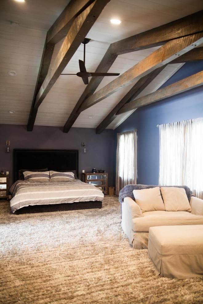 Modelo de dormitorio principal moderno grande con paredes púrpuras, moqueta, chimenea de doble cara, marco de chimenea de madera y suelo gris