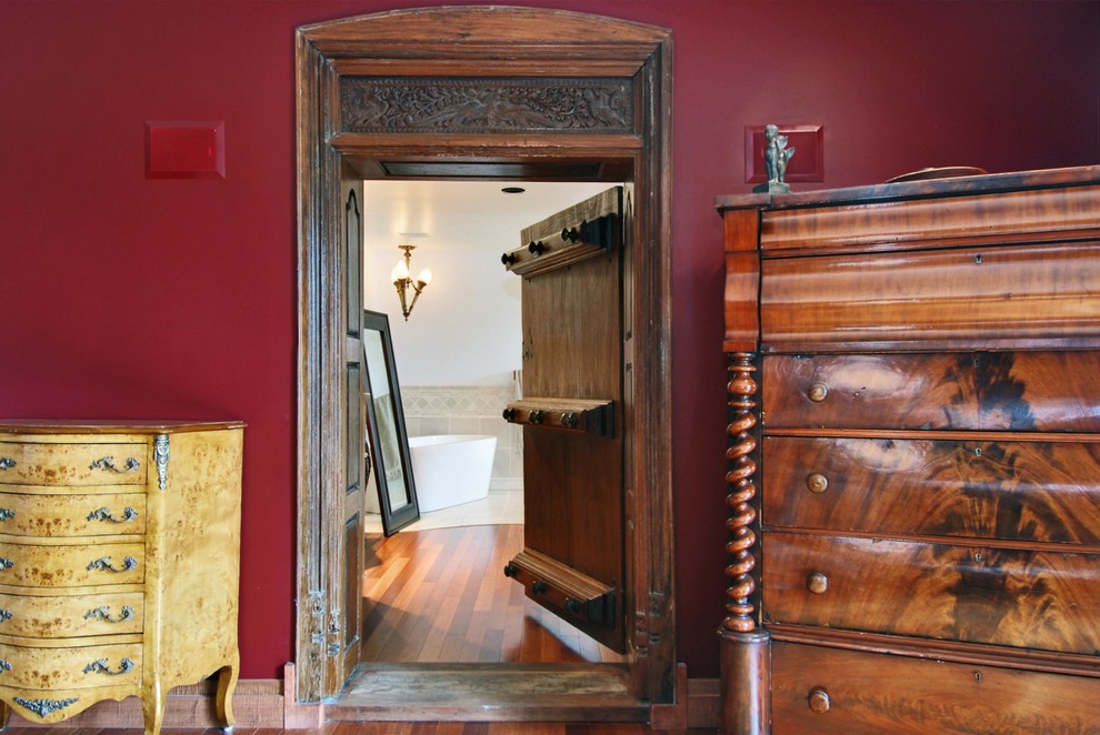 Ejemplo de dormitorio principal actual grande sin chimenea con paredes rojas y suelo de madera en tonos medios