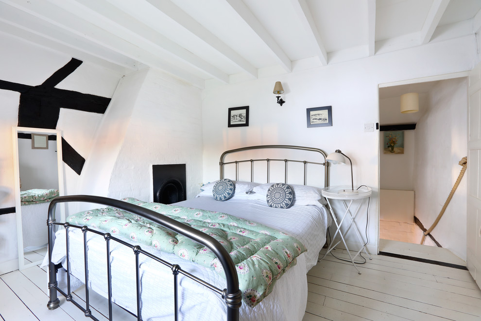 Kleines Landhausstil Hauptschlafzimmer mit weißer Wandfarbe, gebeiztem Holzboden, Kamin und Kaminumrandung aus Backstein in Sussex