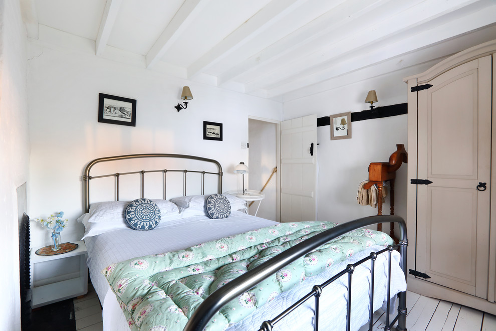 Kleines Country Schlafzimmer mit weißer Wandfarbe, gebeiztem Holzboden, Kamin und Kaminumrandung aus Backstein in Sussex