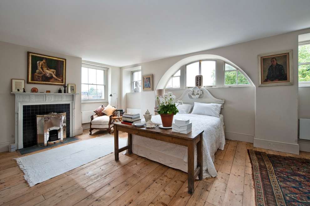 Cette photo montre une grande chambre chic avec un sol en bois brun, une cheminée standard, un manteau de cheminée en carrelage et un sol beige.