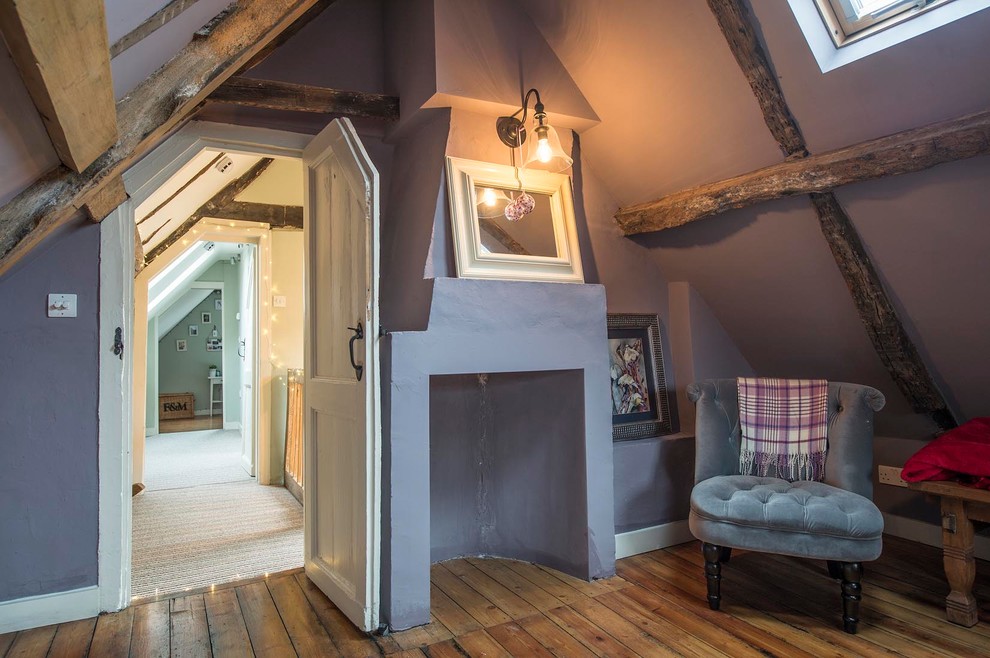Kleines Landhaus Schlafzimmer mit braunem Holzboden, Eckkamin, Kaminumrandung aus Beton und lila Wandfarbe in Sonstige