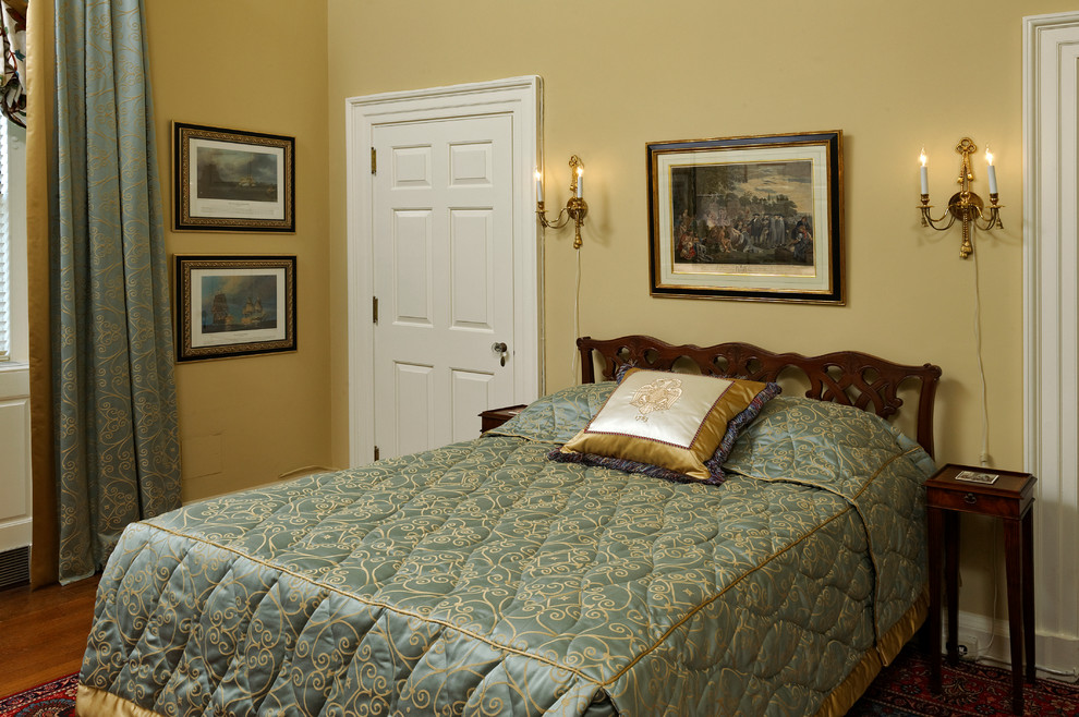 ワシントンD.C.にある中くらいなトラディショナルスタイルのおしゃれな客用寝室 (黄色い壁、無垢フローリング、標準型暖炉、石材の暖炉まわり、茶色い床)