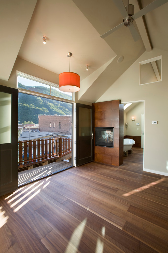 Exemple d'une chambre parentale tendance avec un mur beige, un sol en bois brun, une cheminée double-face et un manteau de cheminée en métal.