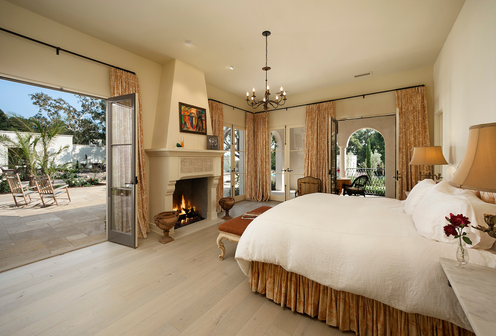 Geräumiges Mediterranes Hauptschlafzimmer mit beiger Wandfarbe, hellem Holzboden, Kamin und verputzter Kaminumrandung in Santa Barbara