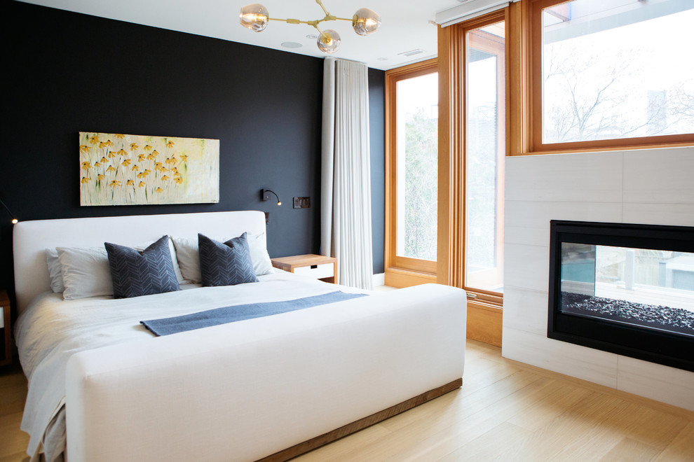 Foto de dormitorio actual con paredes negras, suelo de madera clara, chimenea de doble cara, marco de chimenea de baldosas y/o azulejos y suelo marrón