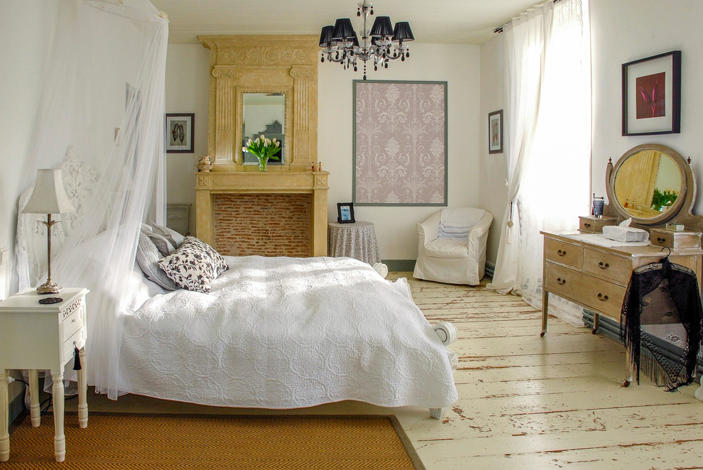 Photo of a medium sized rural guest bedroom in London with white walls, painted wood flooring, a standard fireplace, a stone fireplace surround and white floors.