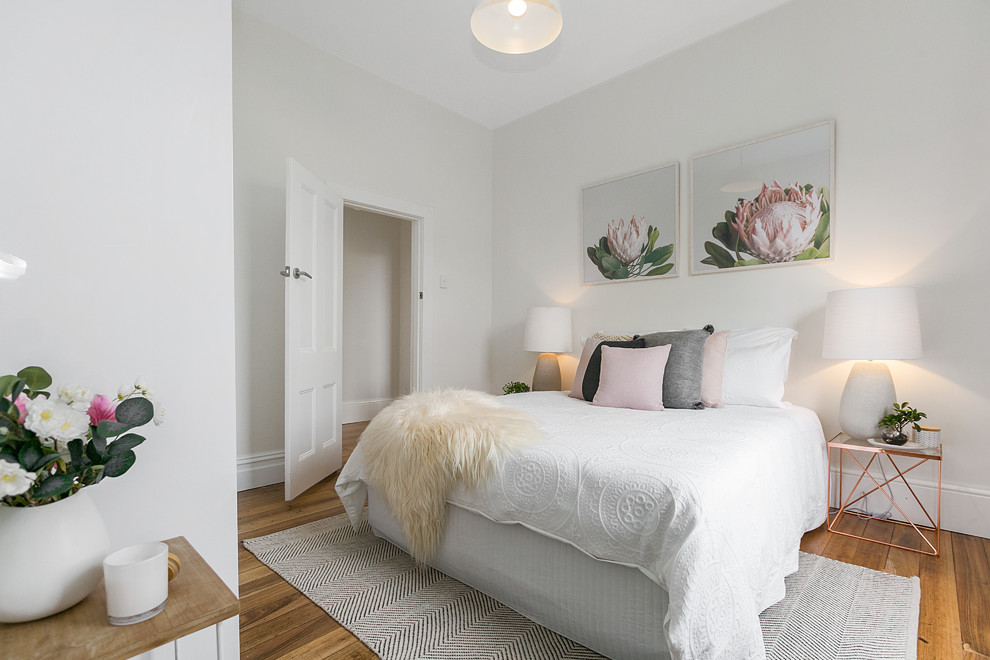 Modelo de dormitorio contemporáneo con paredes blancas y suelo de madera en tonos medios