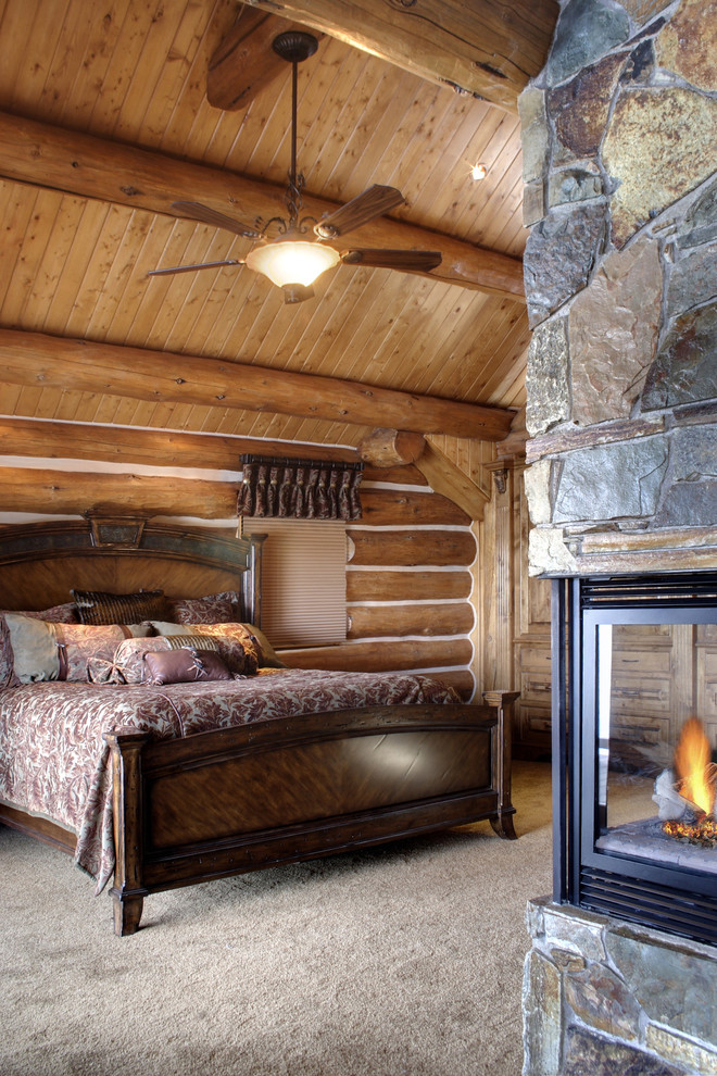 На фото: хозяйская спальня среднего размера в стиле рустика с ковровым покрытием, двусторонним камином, фасадом камина из камня, коричневыми стенами и бежевым полом