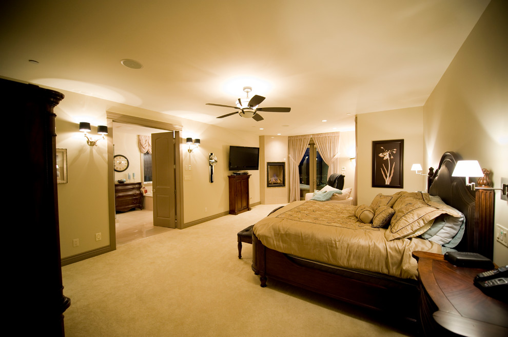 Großes Hauptschlafzimmer mit beiger Wandfarbe, Teppichboden, Eckkamin und verputzter Kaminumrandung in Calgary