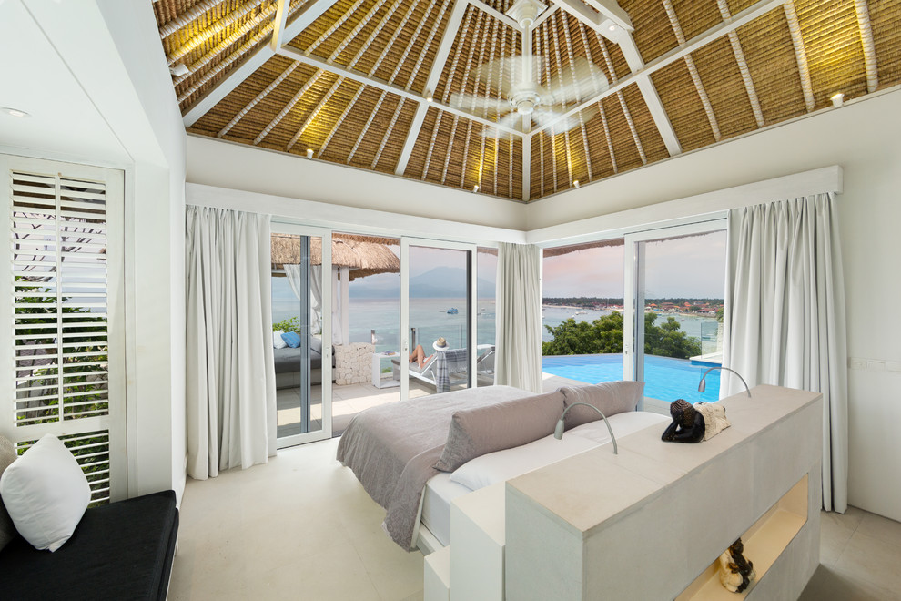 Diseño de dormitorio principal tropical grande sin chimenea con paredes blancas y suelo de piedra caliza
