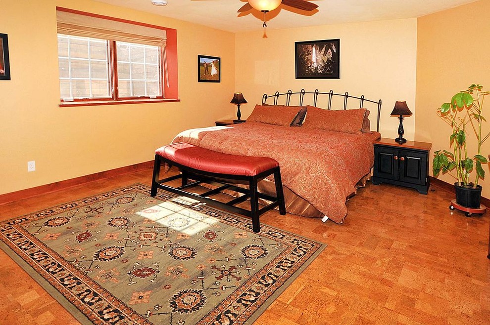 Cette photo montre une chambre d'amis tendance de taille moyenne avec un mur jaune, un sol en liège et aucune cheminée.