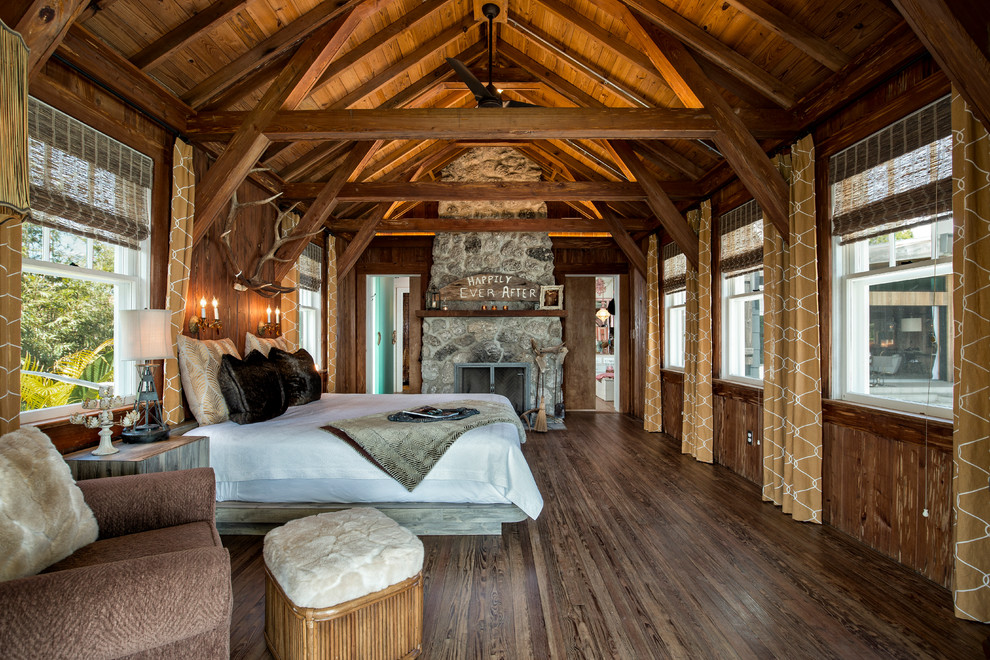 Cette image montre une chambre chalet avec un mur marron, parquet foncé, une cheminée standard, un manteau de cheminée en pierre et un sol marron.