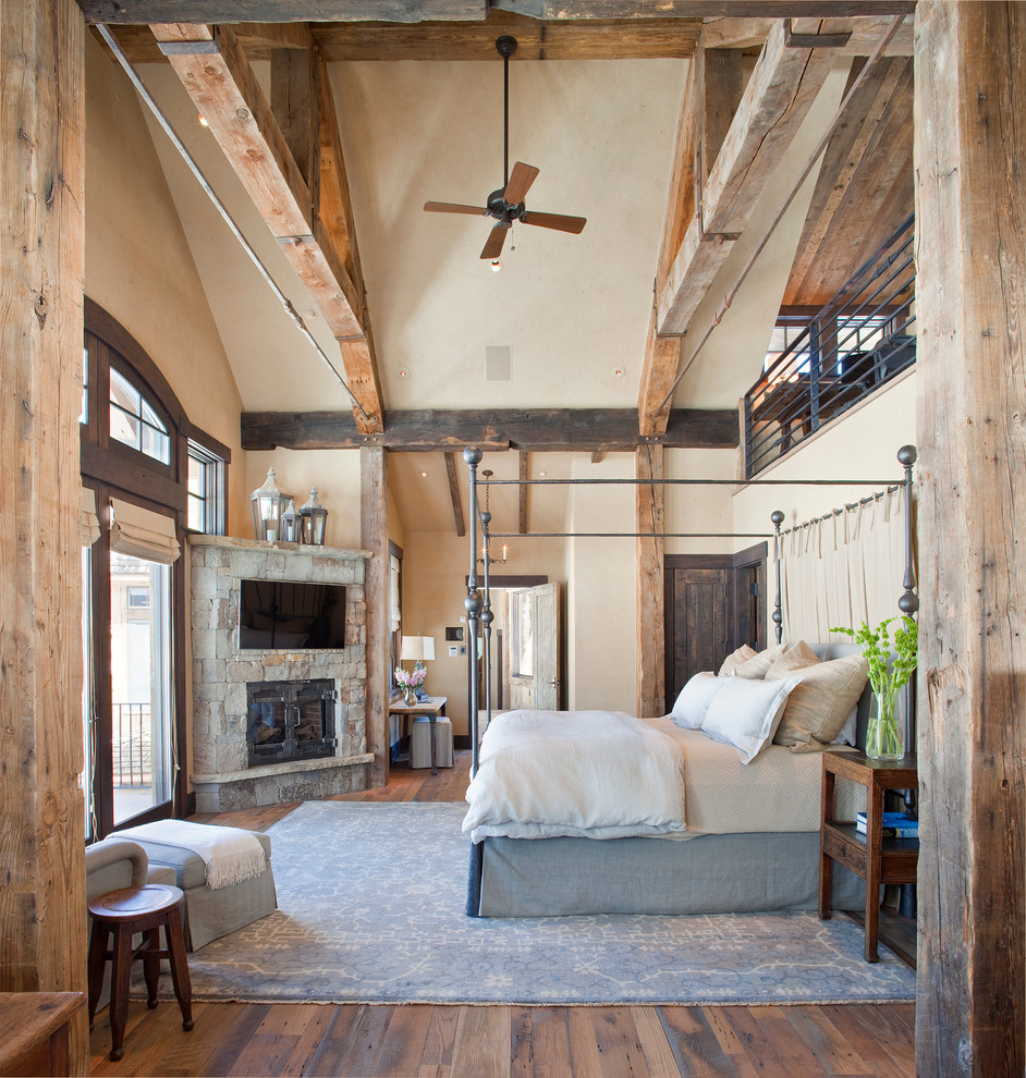 Photo of a large rustic master bedroom in Denver with beige walls, medium hardwood flooring, a corner fireplace, a stone fireplace surround and feature lighting.