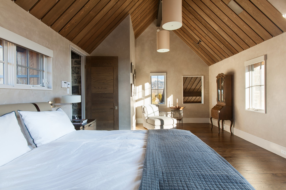 Modelo de dormitorio principal rural sin chimenea con paredes beige y suelo de madera oscura