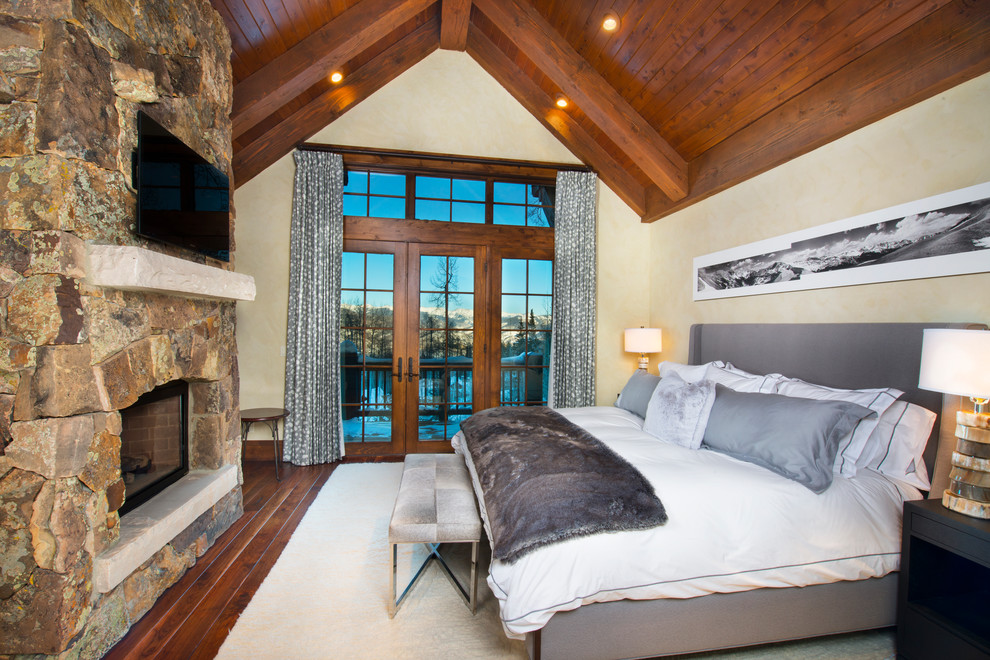 Foto de dormitorio rural con paredes beige, suelo de madera oscura, todas las chimeneas y marco de chimenea de piedra