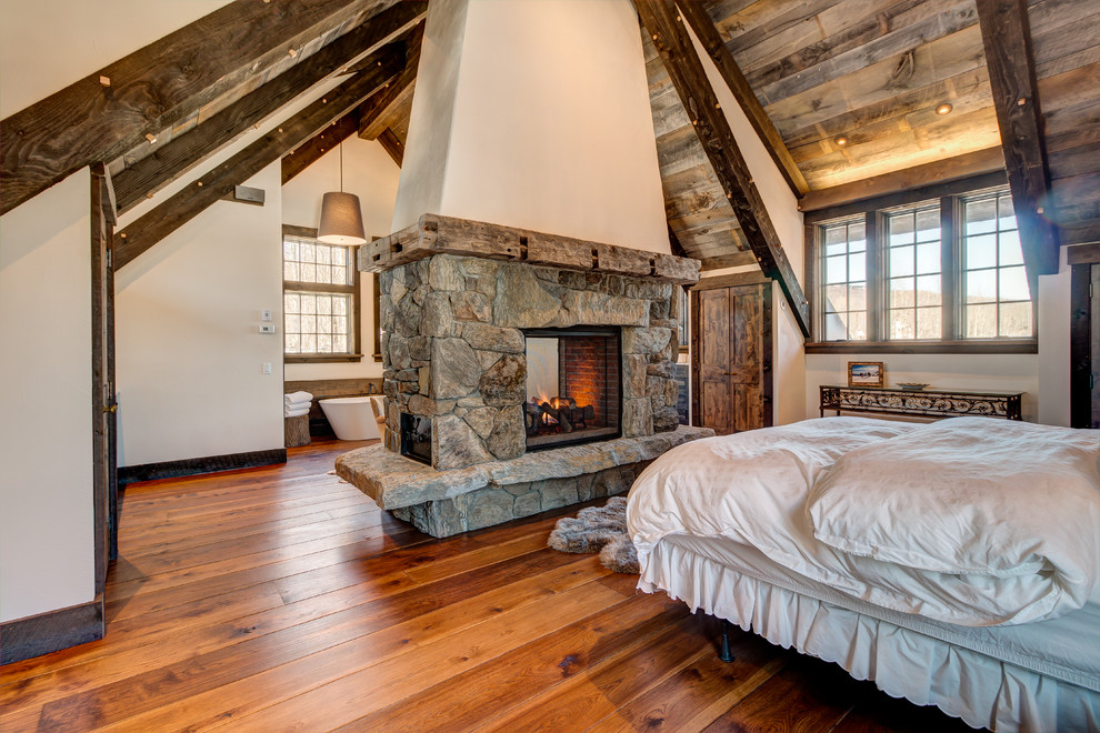 Cette photo montre une chambre parentale montagne avec une cheminée double-face et un manteau de cheminée en pierre.