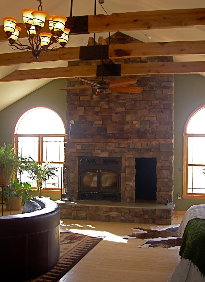 シャーロットにある広いラスティックスタイルのおしゃれな主寝室 (緑の壁、竹フローリング、薪ストーブ、石材の暖炉まわり)