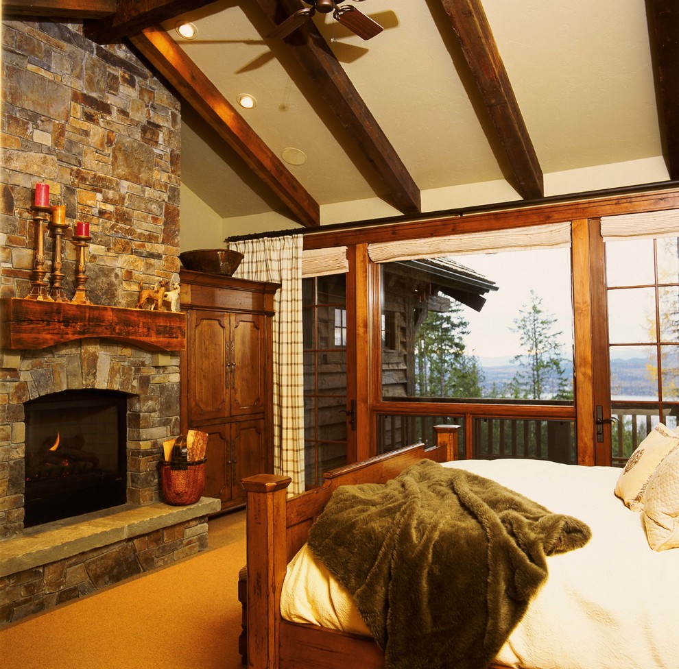 Photo of a large rustic master bedroom in Denver with beige walls, a standard fireplace and a stone fireplace surround.