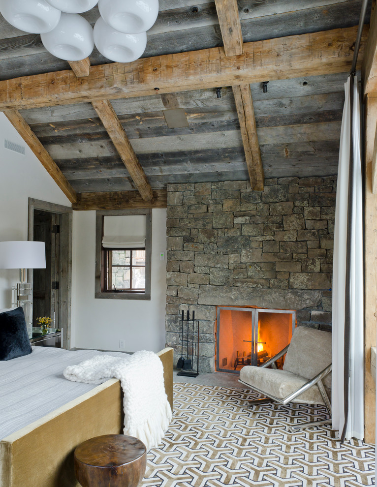Ejemplo de dormitorio rústico con paredes blancas, todas las chimeneas y marco de chimenea de piedra