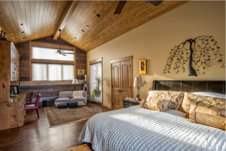 Modelo de dormitorio principal rural grande sin chimenea con paredes amarillas, suelo de madera en tonos medios y suelo marrón