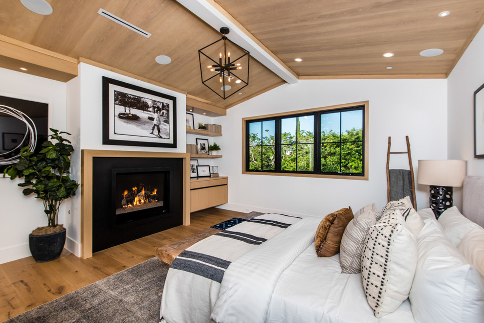 Example of a transitional medium tone wood floor and brown floor bedroom design in Los Angeles with white walls and a standard fireplace
