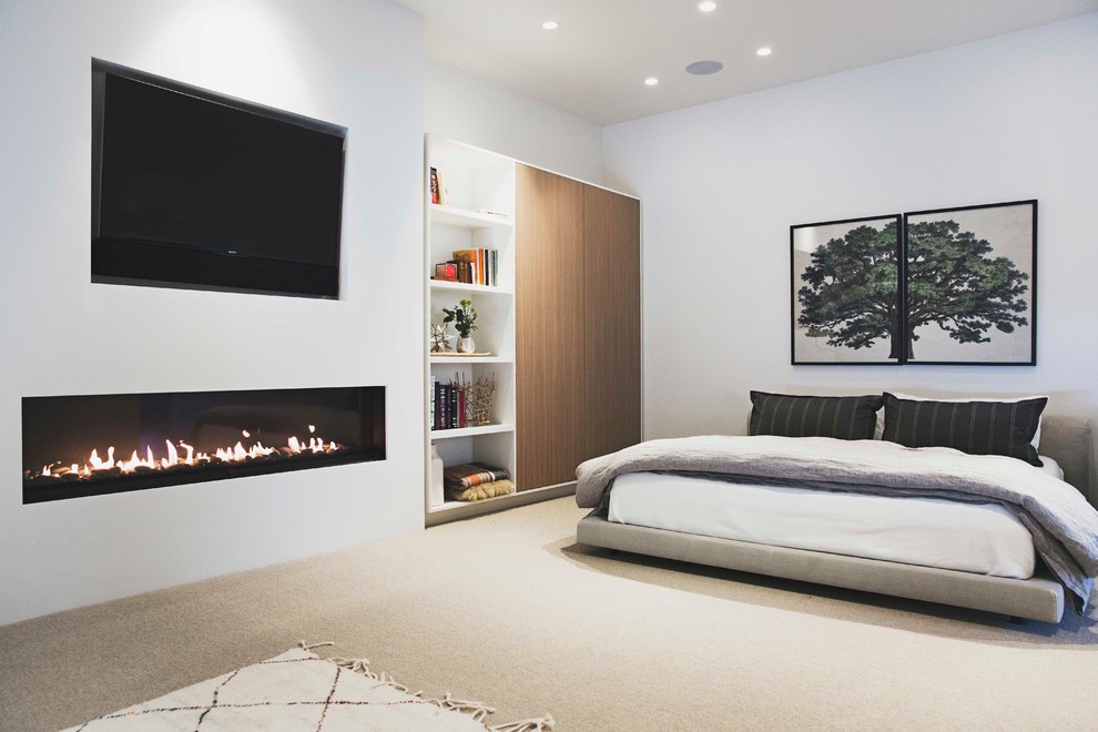 Cette image montre une grande chambre minimaliste avec un mur blanc, une cheminée ribbon, un manteau de cheminée en plâtre et un sol gris.