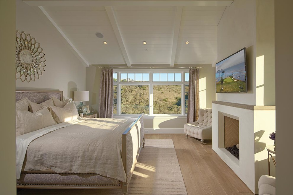 This is an example of a coastal master bedroom in Orange County with beige walls and light hardwood flooring.
